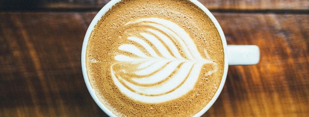 A cup sits on a table filled with an artisan cappuccino and foaming milk