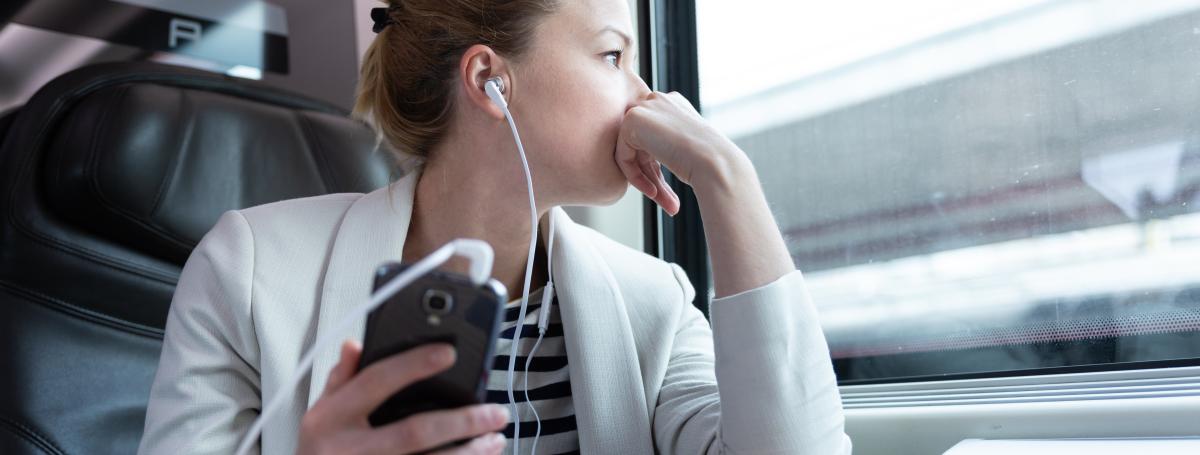 A woman has earbuds in and listens to a podcast on her smartphone.