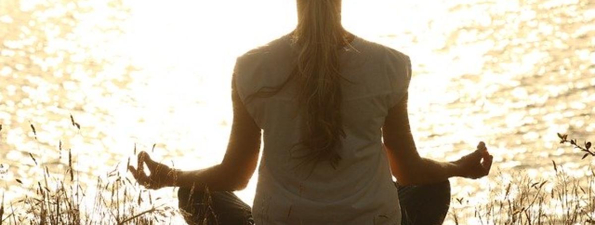 A woman sits in a cross legged yoga position with her hands in front of her in prayer.