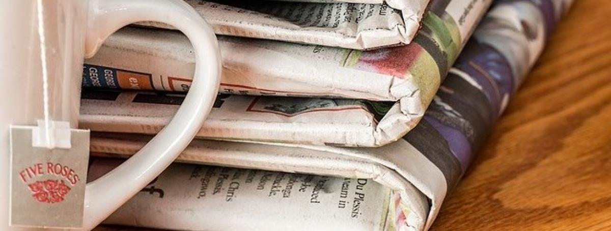 Three folded newspapers sits on a table next to a cup of tea.