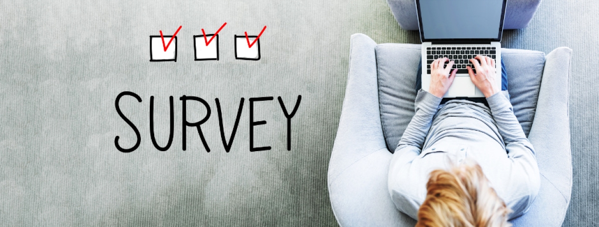 A woman sits on a chair with her laptop on her lap. To the left of the chair is a superimposed graphic of three checked boxes.Text: Survey.