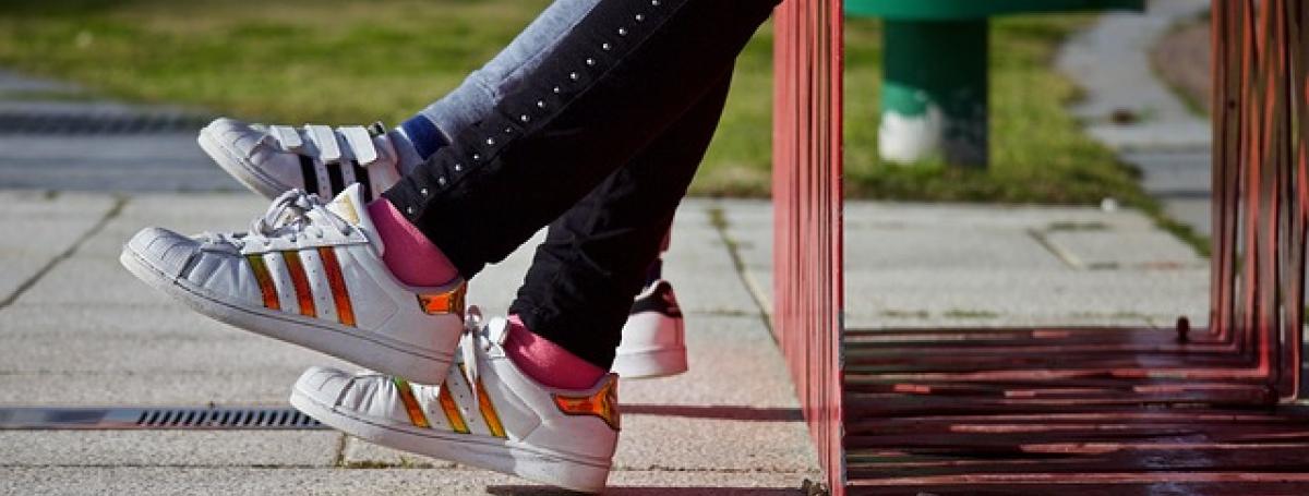 The feet of two teenagers dangle off of an outdoor bench.