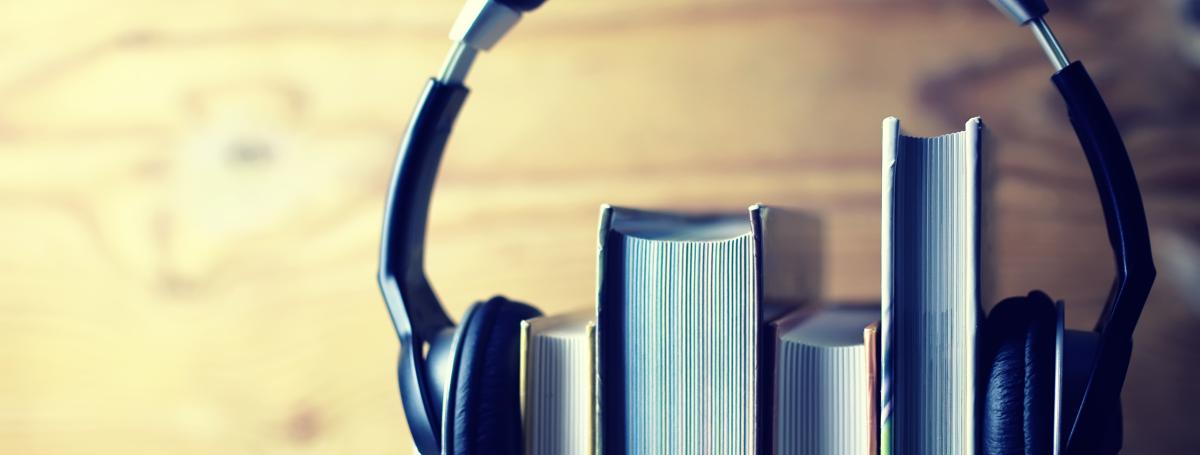 A stack of four books sits on a shelf. A pair of headphones sits on top of the books - holding them together.