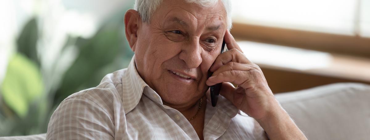 An elderly man talks on a smartphone. 
