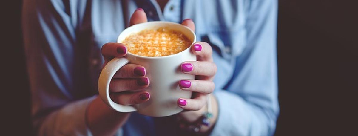A woman's hands firmly grip a piping hot cup of coffee.