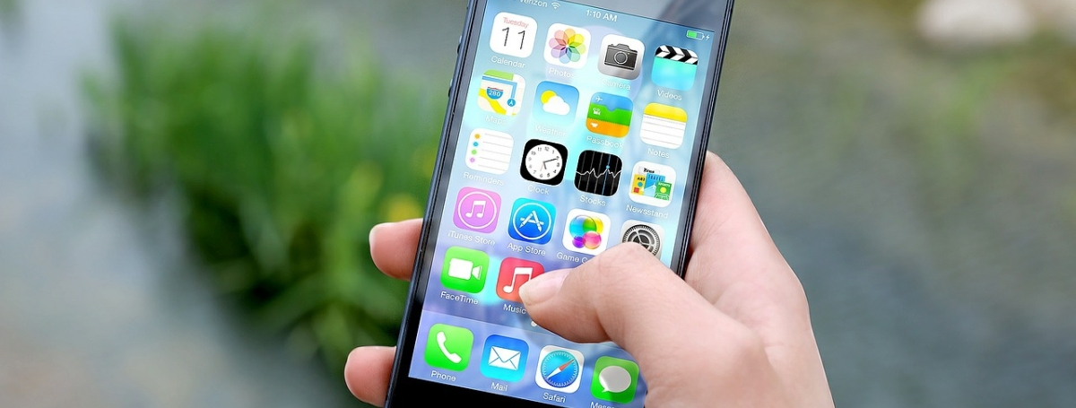 une main tenant un iPhone, on voit la page avec toutes les applications.