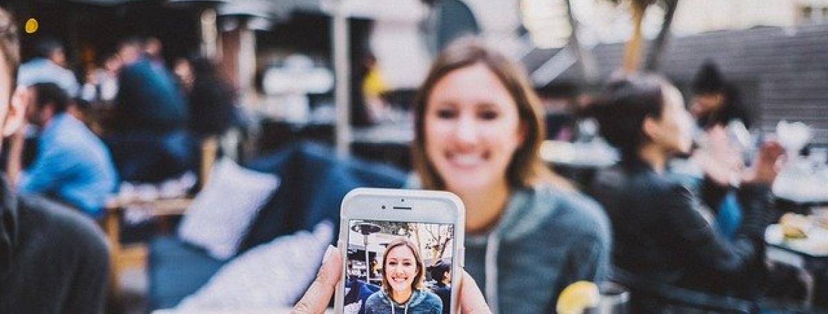 Two women dining. One woman takes a picture of her friend with her smartphone.