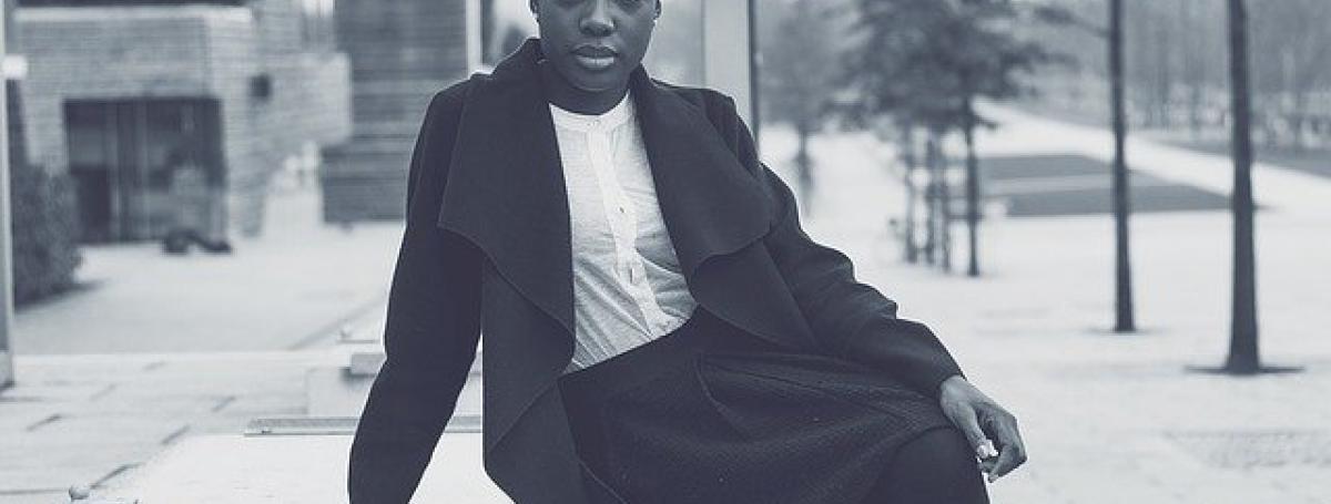 A young woman poses on an outdoor ledge. She is wearing business casual attire.