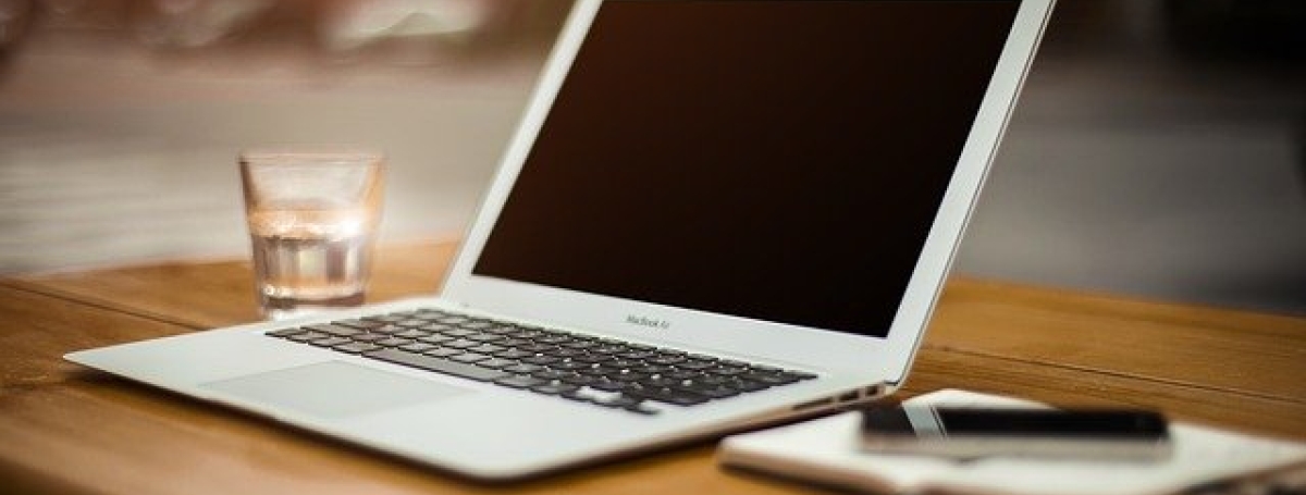 A laptop computer sits on top of a work-from-home kitchen table environment.