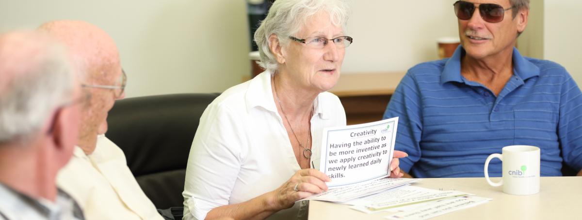 A peer support group featuring four elderly people sitting around a table drinking coffee.