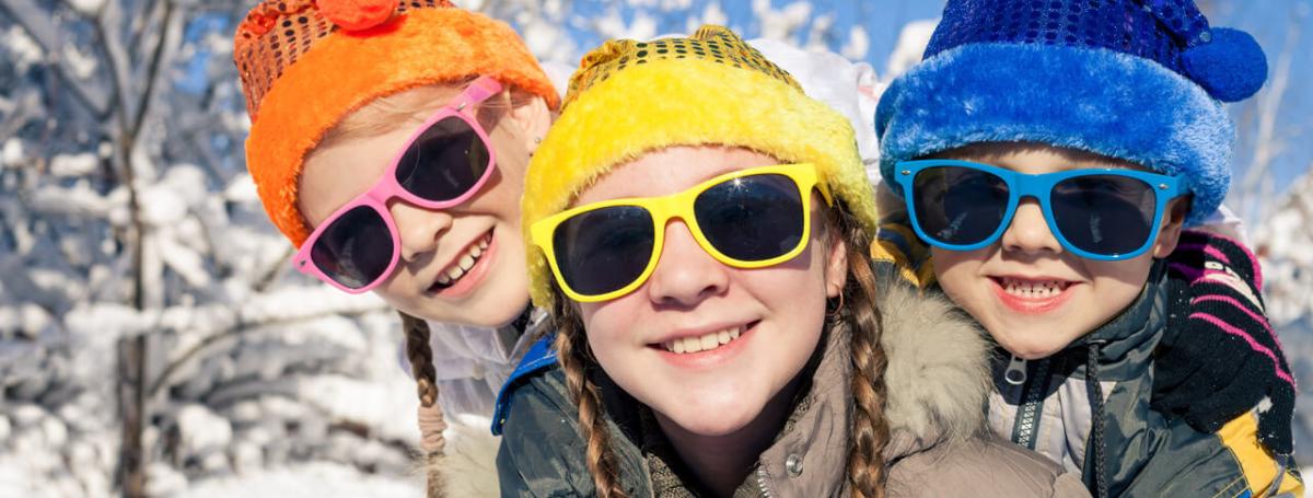 Three children outside in the snow wearing colourful hats and sunglasses