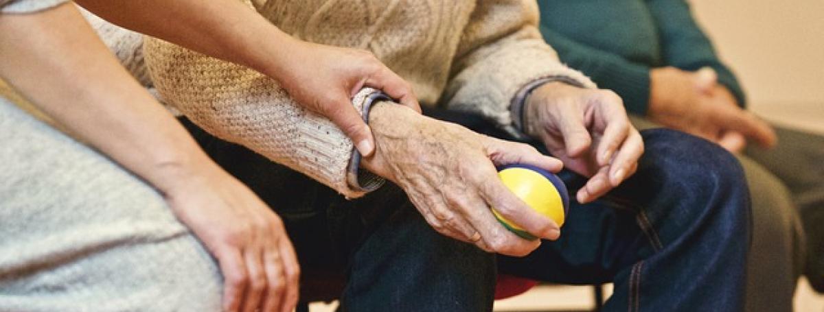The hands of an elderly man squishing a stress ball.