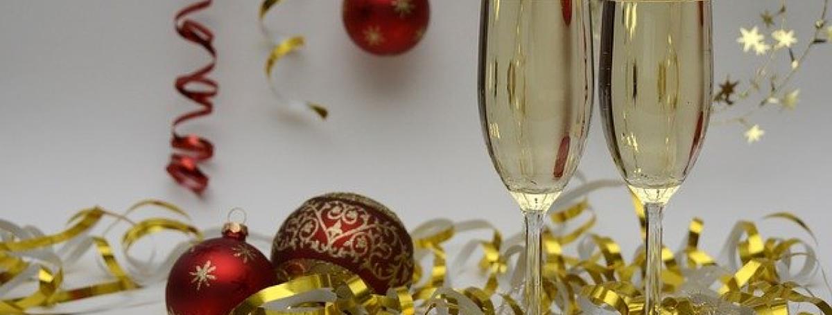 Two glasses of champagne sit on a table which is littered with Christmas bulbs, glitter and ribbon.