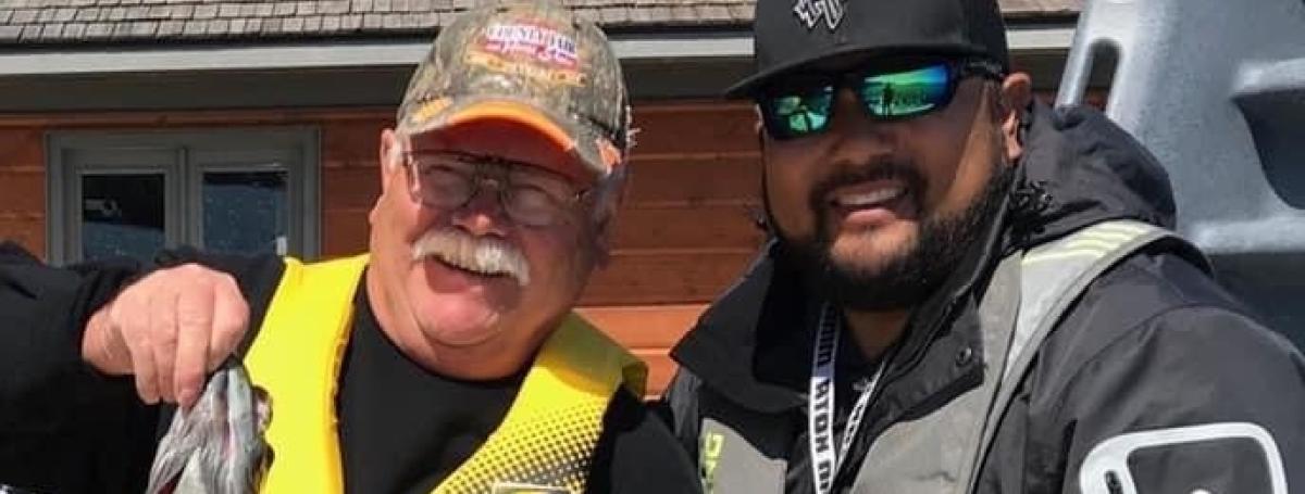 Camper Bruce holding a fish, standing beside Eugene Chong on the Boathouse dock.