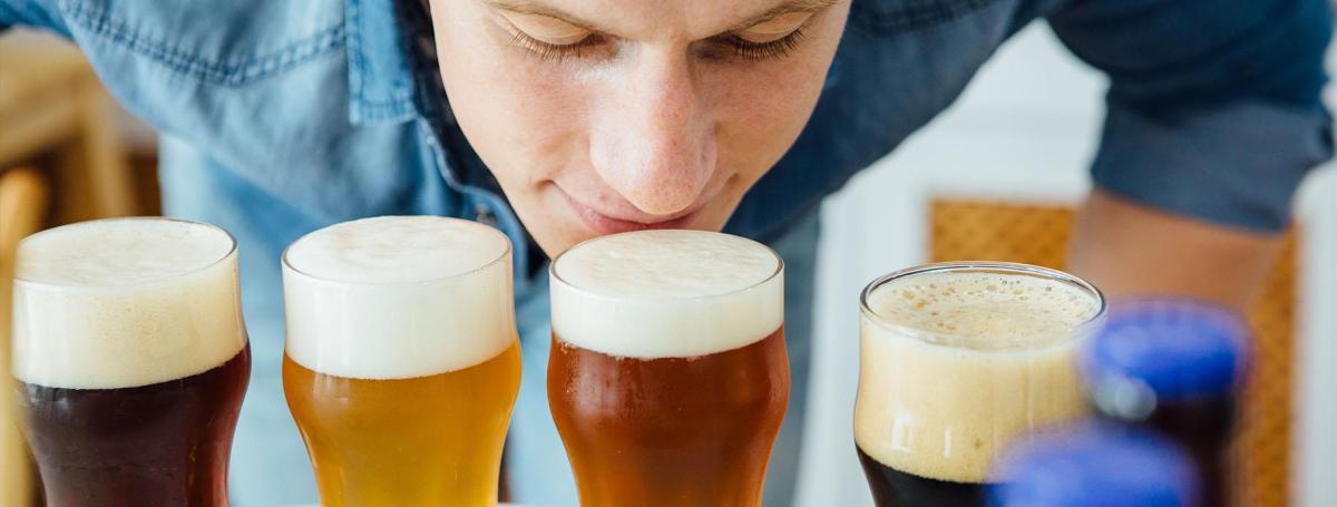 Man bending over to sniff one of four full glasses of beer.