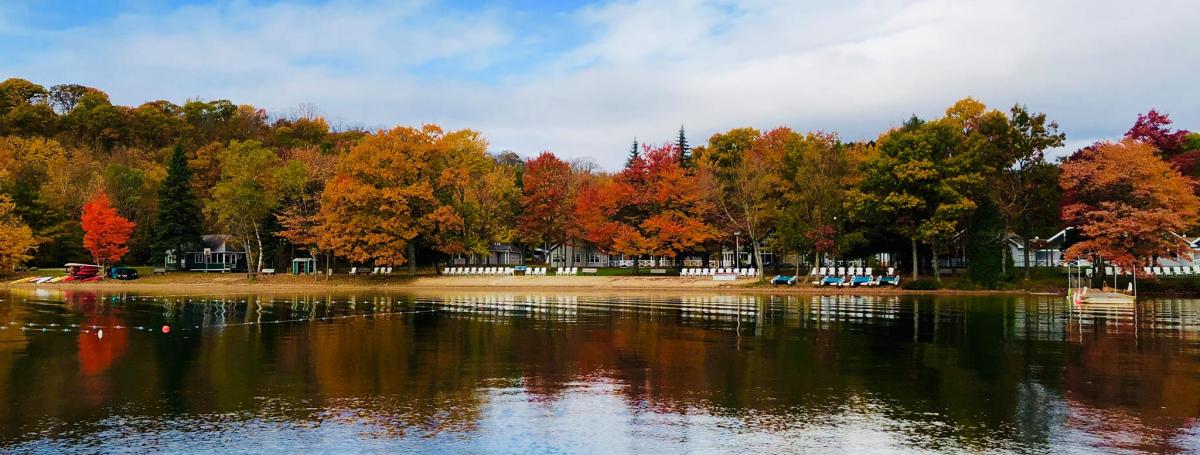 View of CNIB Lake Joe from the water with the bright blue sky reflected in the water and the trees turning red and orange.