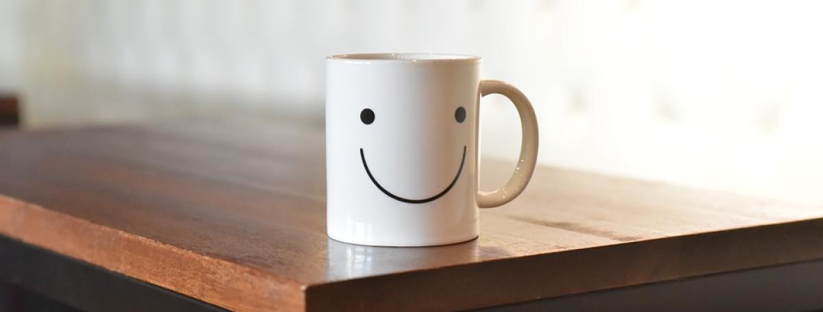 White coffee mug with a smiley face on it, sitting on a wood table