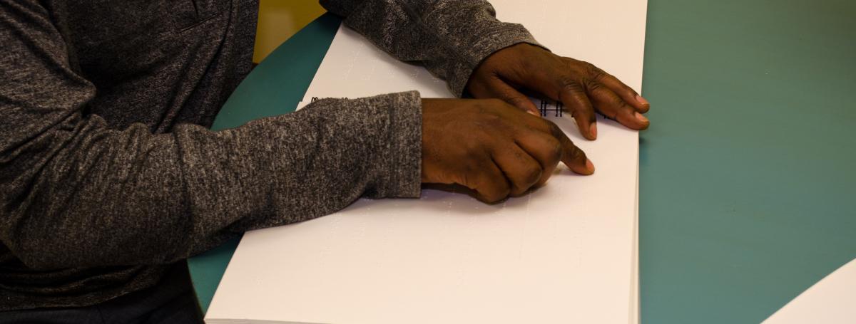 Reading a braille book. Hands glide over a brailled book.