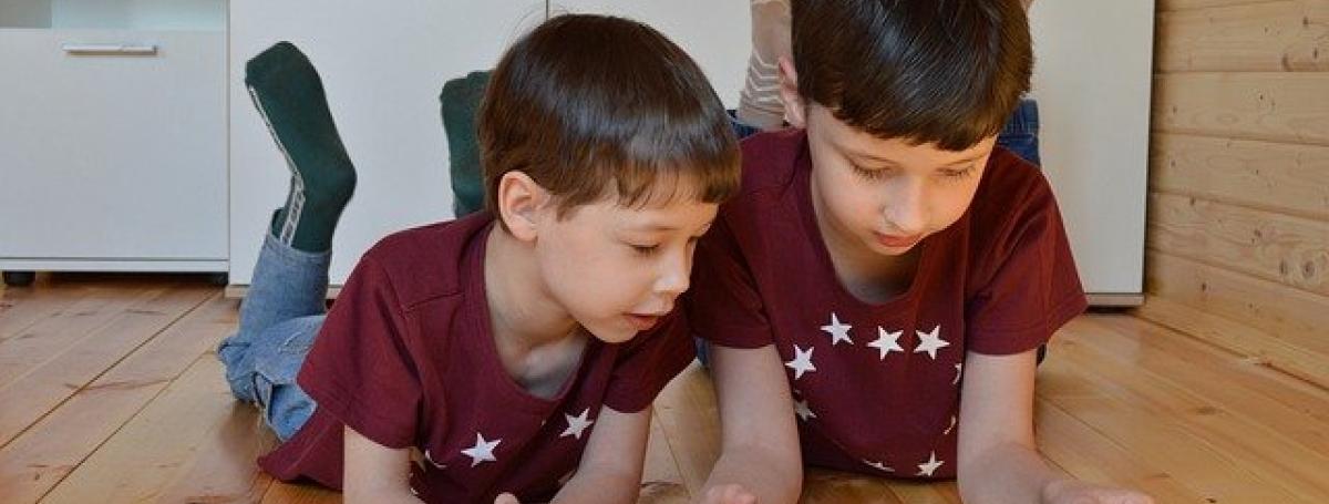 Two young brothers sit on their bedroom floor and interact with an iPad.
