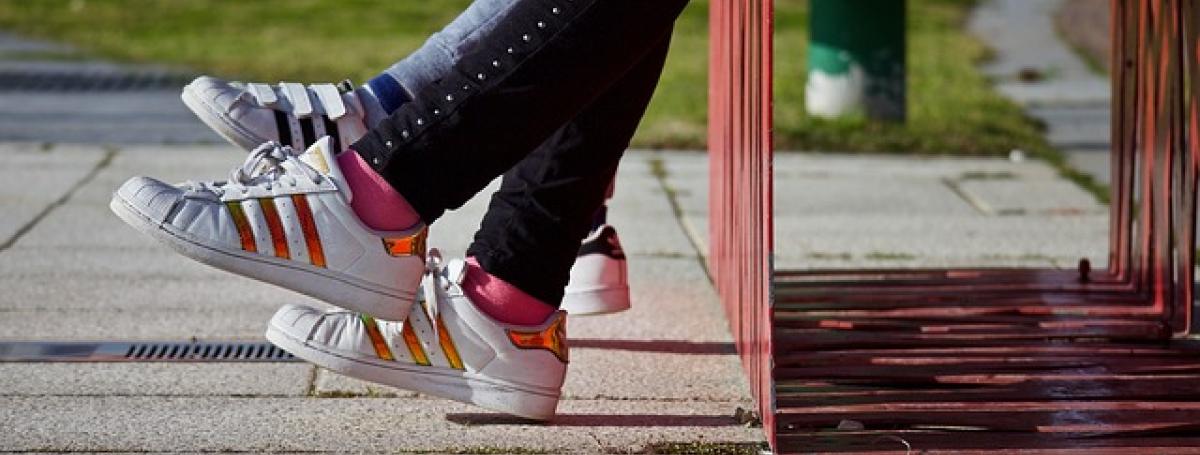 The shoes of two young people sitting outdoors on a bench.