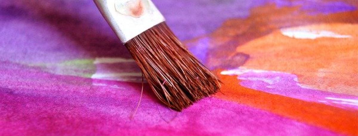 A paintbrush paints a watercolour design on a piece of paper.