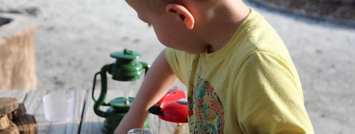A young boy holds a magnifying glass and plays at a table.