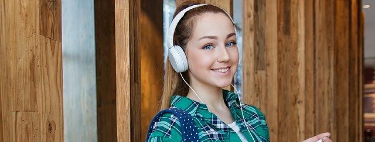 A young female student wears a backpack and headphones. The headphones are connected to her iPhone.
