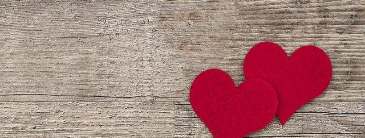 Two tiny red hearts made of construction paper sit on top of a wooden table.