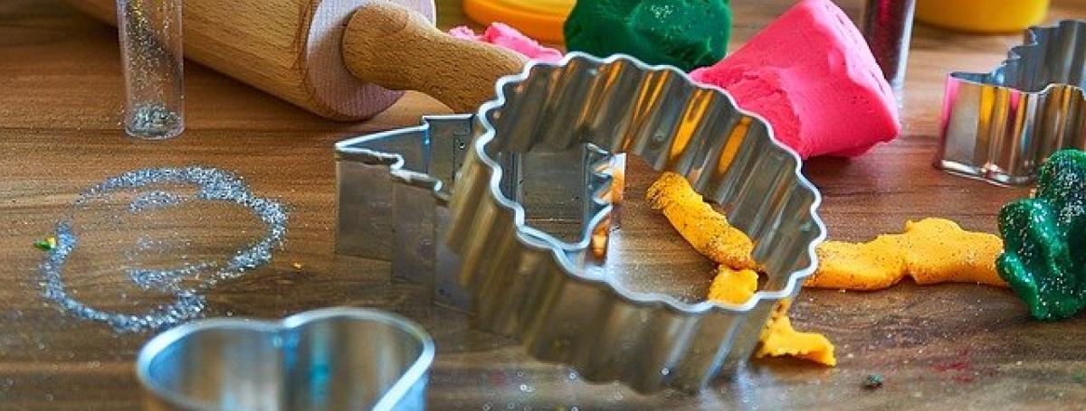 Cookie cutters, a rolling pin and colourful playdough sit on a kitchen table top.