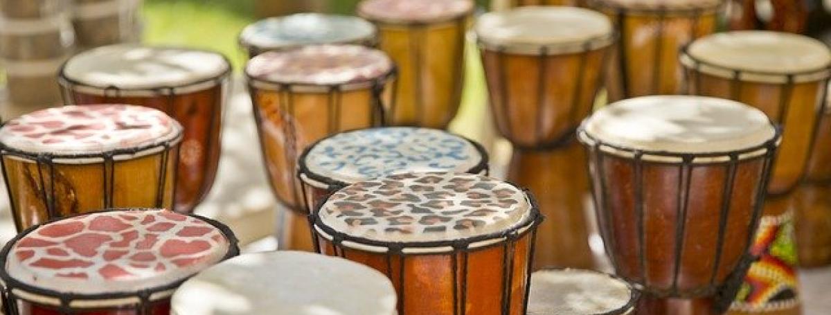 Multiple Djembe Drums sit outdoors on pavement ready to be played.