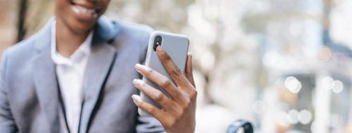 Femme noire assise sur un banc de parc, portant une veste d'affaires et tenant son téléphone intelligent.