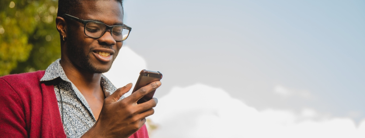 Un homme regardant la cellulaire dans sa main est dehors sous un ciel bleu et partiellement nuageux