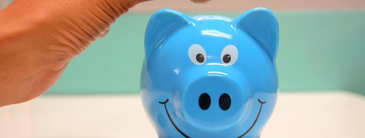 Une main, à gauche, tient un pièce de monnaie au-dessus d'une tirelire bleue.