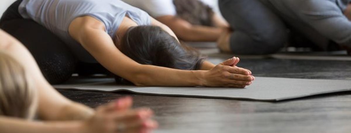A yoga class. Three people kneel in a yoga position on their yoga mats.