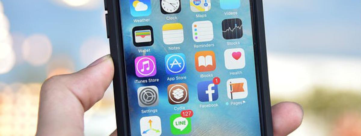 A hand holds an iPhone. The screen is illuminated with various apps.
