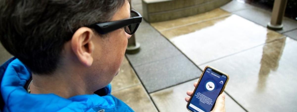 A woman holds an iPhone in her hand. On the screen, the Soundscape app is open.