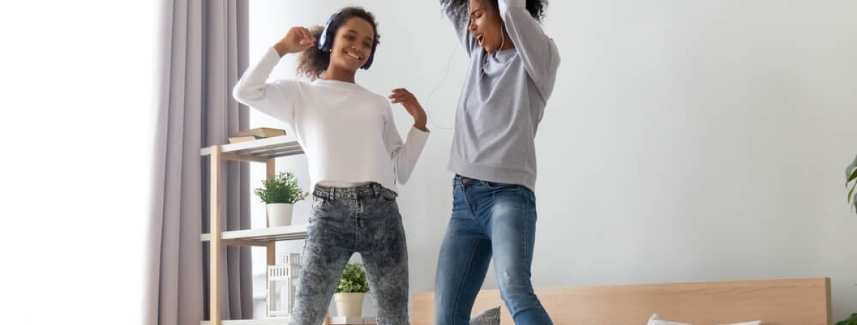 Two teenage girls singing and dancing on a bed.
