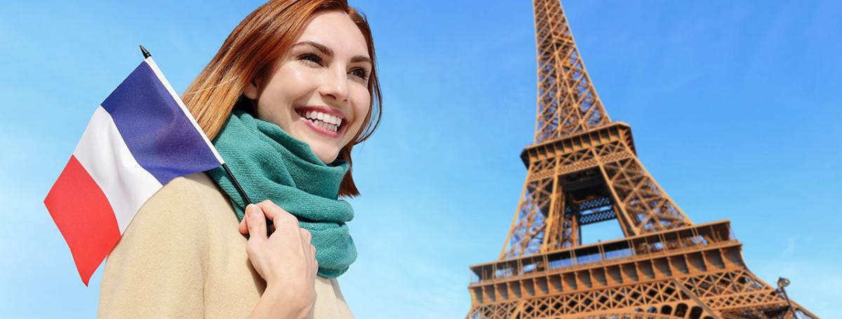 Smiling woman holding the French flag in front of the Eifel Tower.
