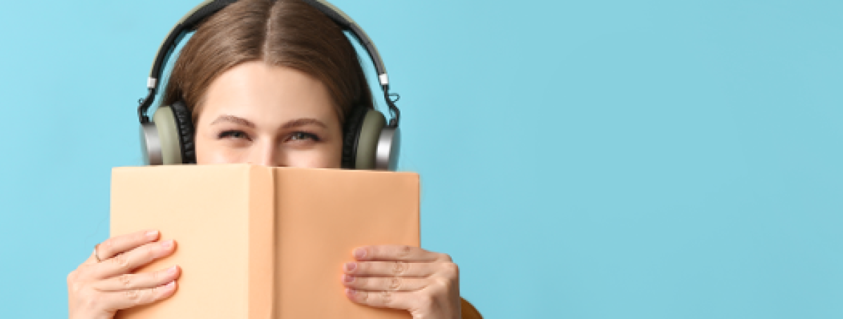 Une femme portant un casque d'écoute tient un livre dans ses mains.