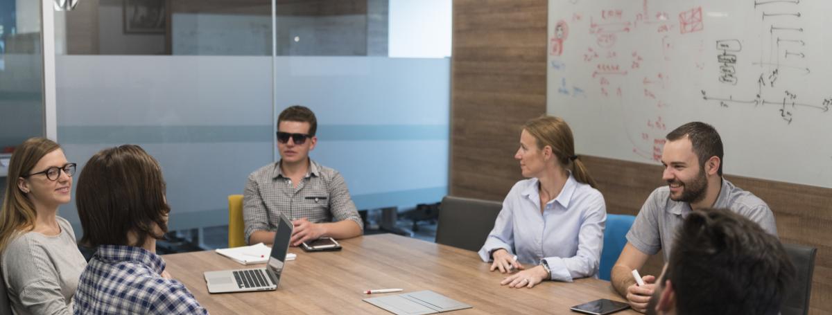A meeting in a boardroom. Six people gather around a table.