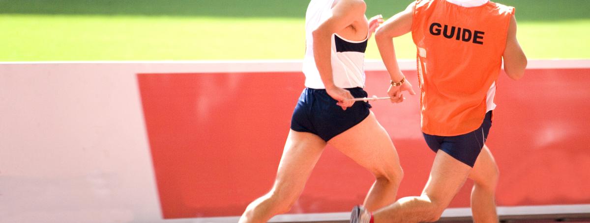 A man runs on a track course alongside a guide runner.