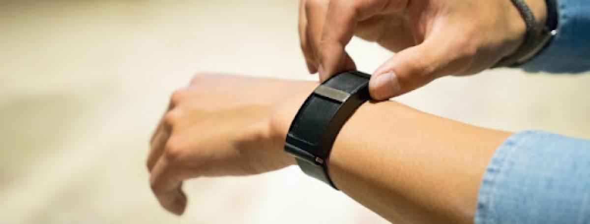 An arm displays the Wayband device around its wrist.