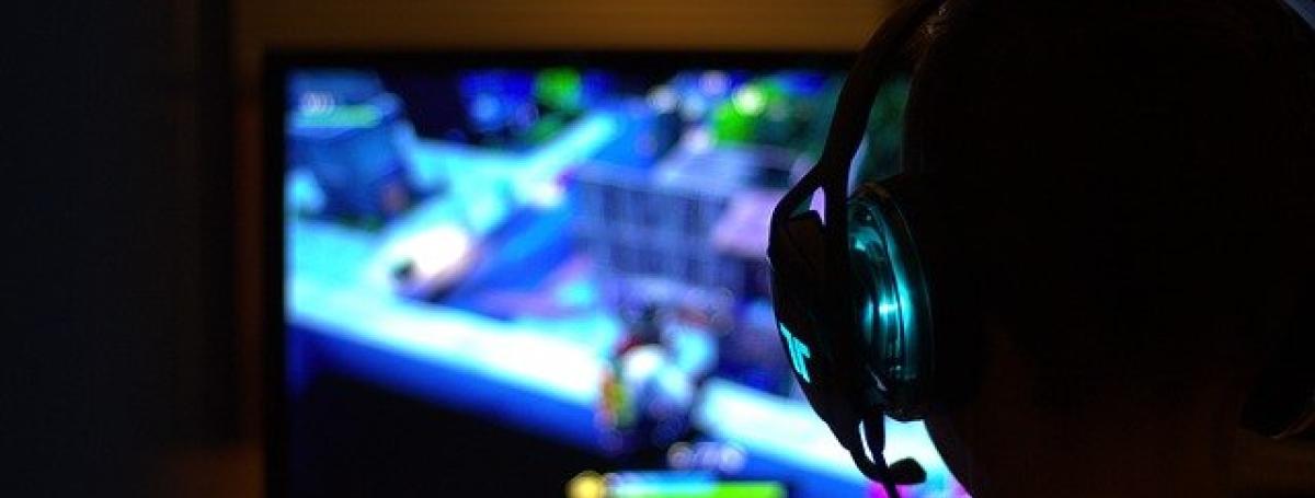 A gamer wearing a headset with a microphone sits in front of a computer monitor.