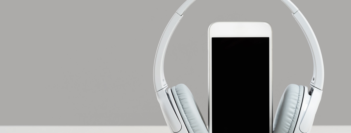 A smartphone sits vertical on a table. Wireless headphones rest on the exterior of the phone.
