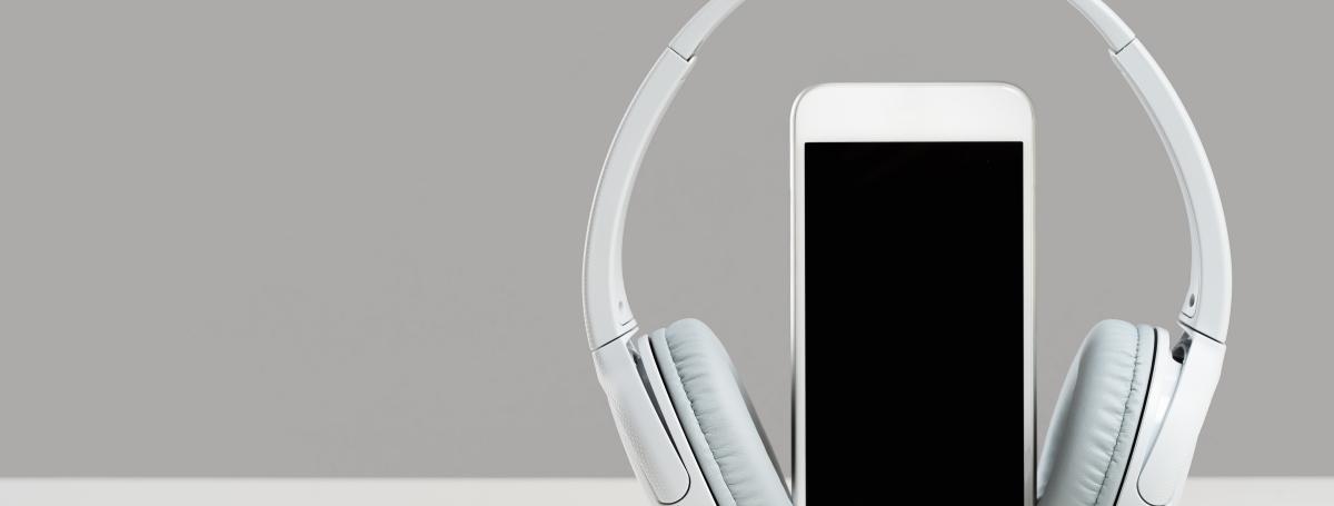 A smartphone sits vertical on a table.  Wireless headphones rest on the exterior of the phone. 
