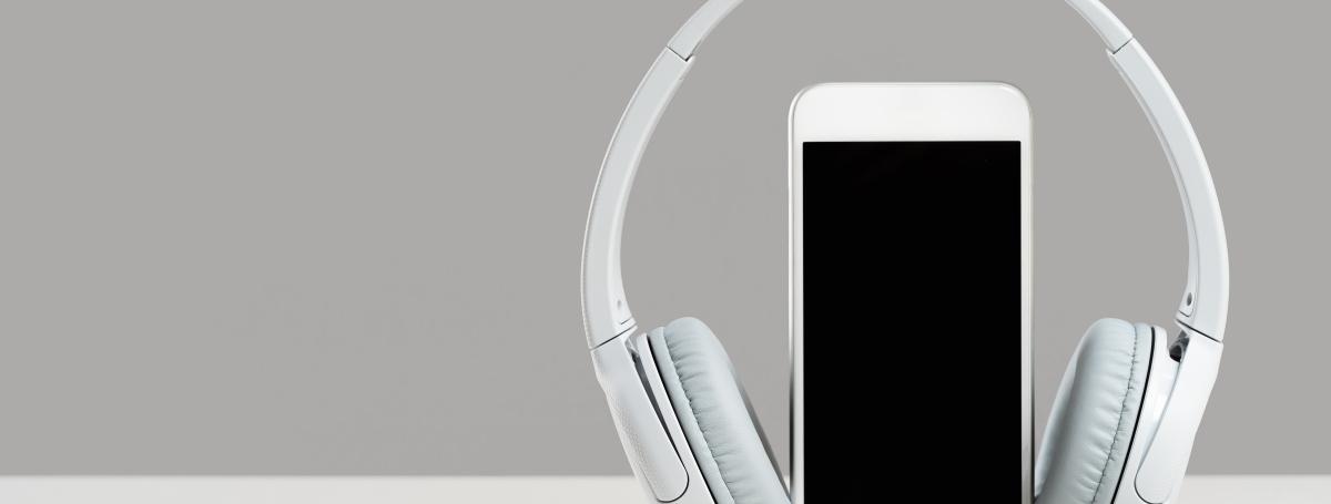 A smartphone sits vertical on a table. Wireless headphones rest on the exterior of the phone.
