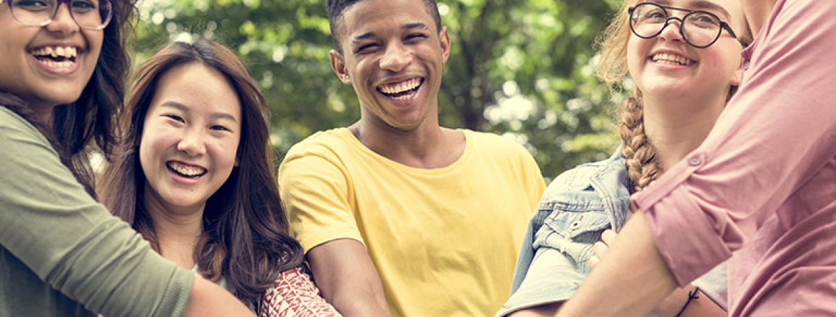 Photo de jeunes de diverses origines se tenant à l'extérieur, les bras tendus pour se donner la main.