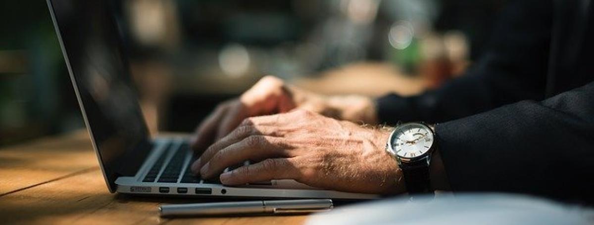 An elderly mans hands on a laptop keyboard.