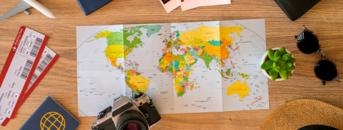 Map, camera, passport, plane tickets, photos, sunglasses and hat on top of a table