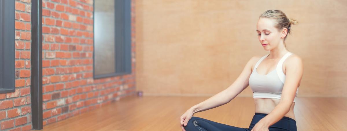 Une femme assise les jambes croisée en lotus sur un tapis de yoga.